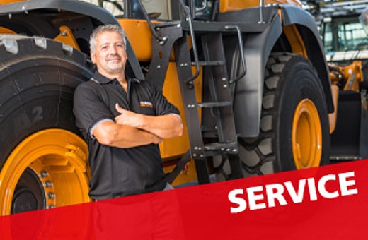 Servicemitarbeiter steht vor einem großen gelben Radlader in der Werkstatt