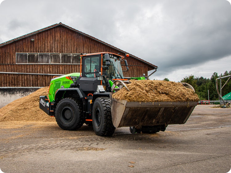 LiuGong 838TE mit einer vollen Schaufel Silage vor einer Halle.
