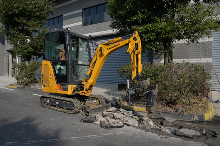 Gelber LiuGong Minibagger mit Kabine und Gummiketten bearbeitet eine Straße