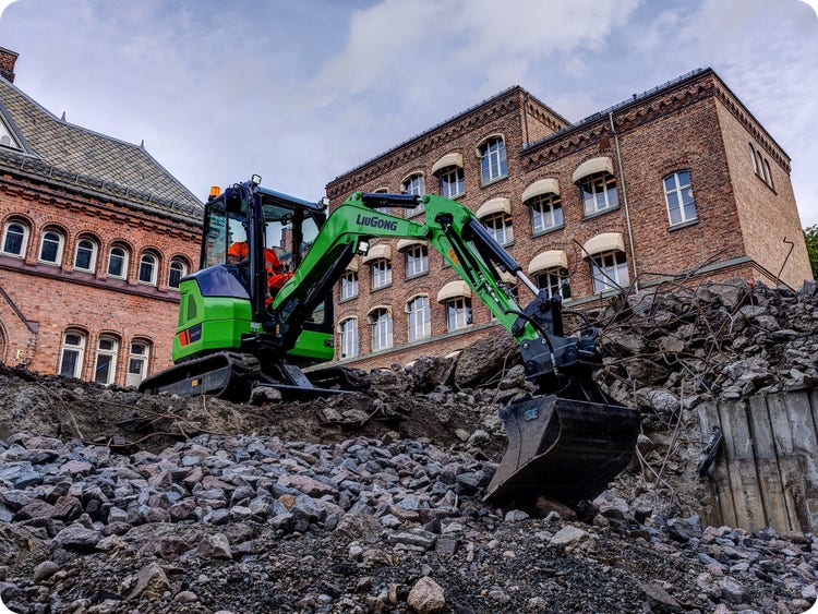 LiuGong 9027FE in einer Baugrube mit einem Backsteingebäude im Hintergrund.